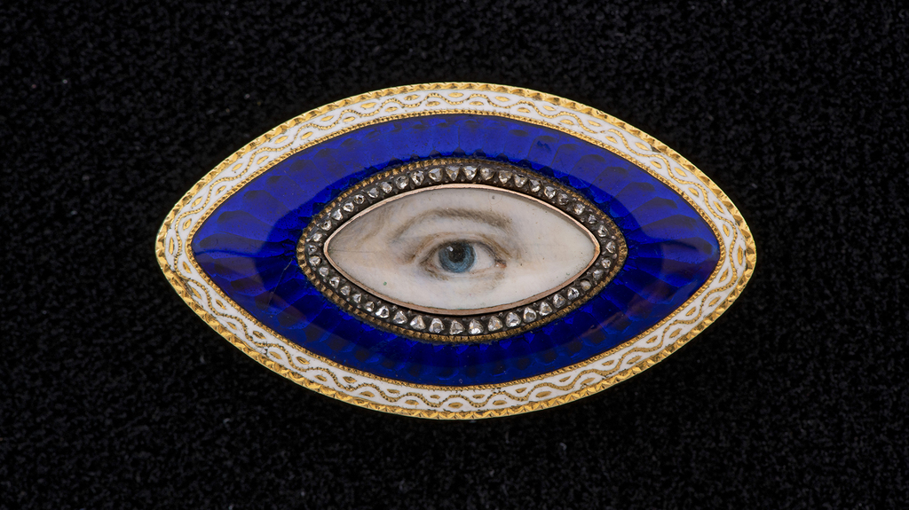 A gold oval Lover’s Eye brooch with a band of diamonds within a blue glass guilloche border surrounded by white enamel, 1890
